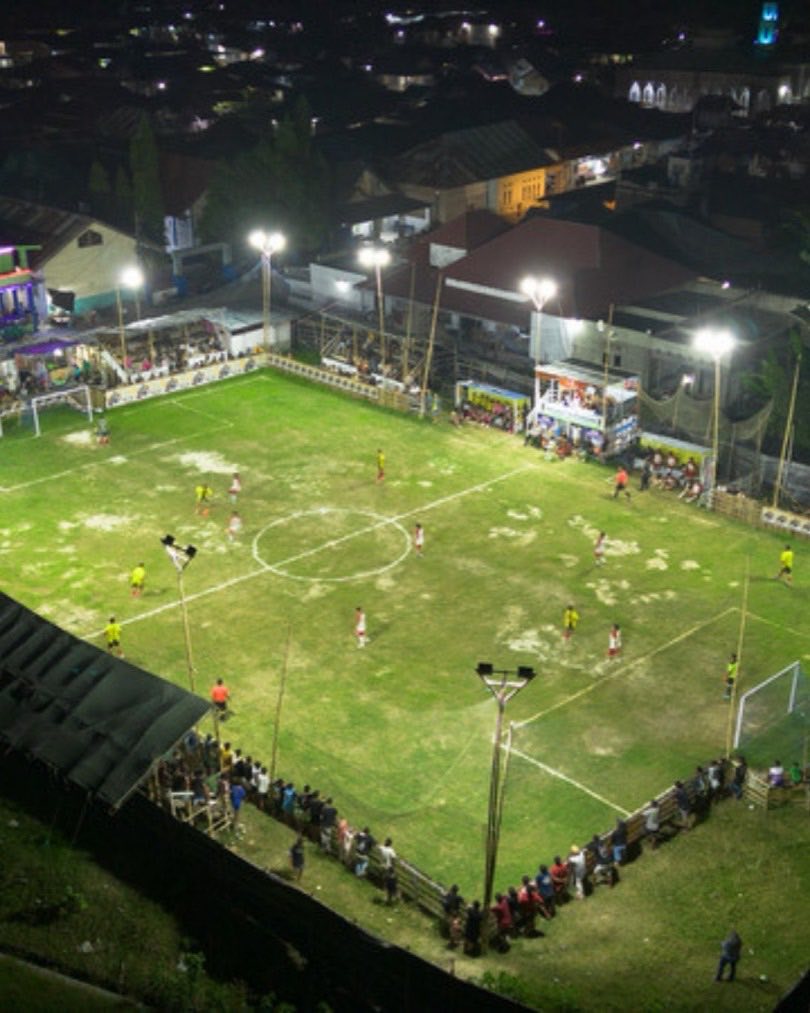 Sportplatz bei Flutlicht von oben, Zuschauer stehen am Spielfeldrand