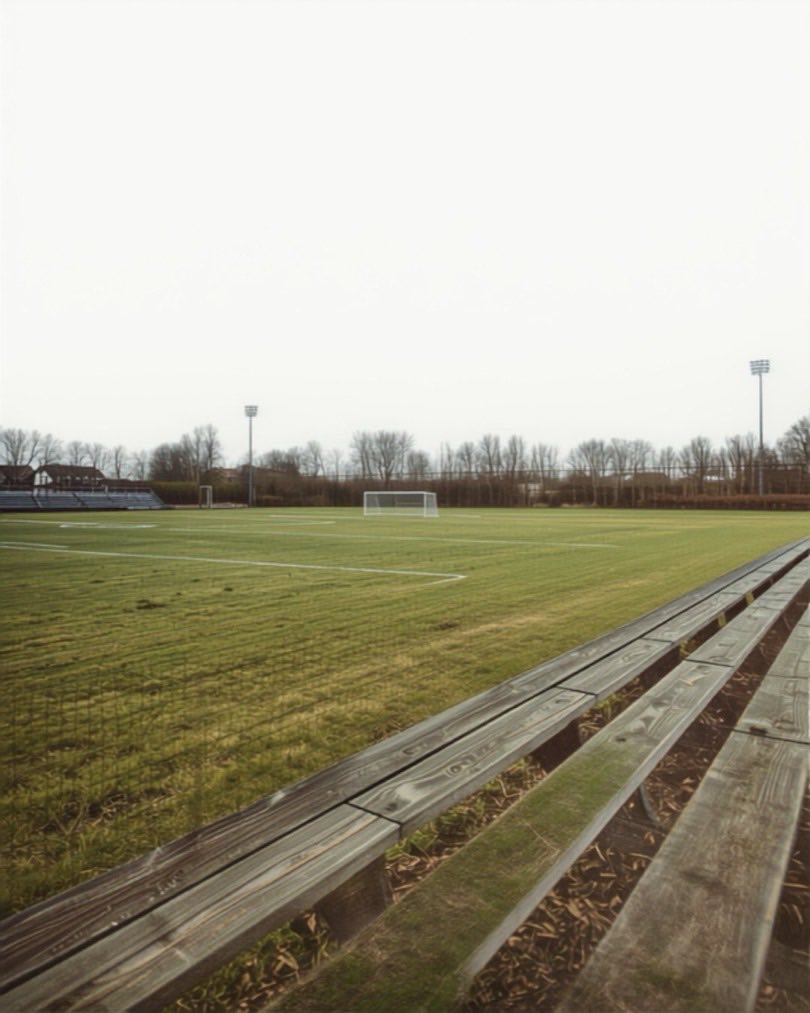 Leere Holzbänke am Rand eines Sportplatzes an einem trüben Tag